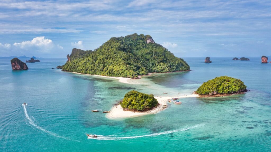 Aerial panorama of Krabi’s tropical islands and sandbar linking islets, with boats cruising over crystal-clear Andaman waters.